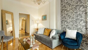 Ein modernes Wohnzimmer mit einem grauen Sofa, einem blauen Sessel, einem Glastisch und einer Deckenleuchte.