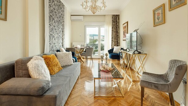 Ein modernes Wohnzimmer mit einem grauen Sofa, einer TV-Kommode und einem Essbereich mit Tisch und Stühlen.