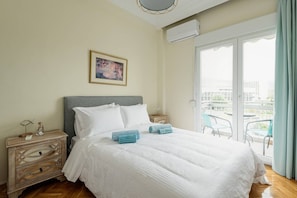 A bedroom with a bed, a nightstand, a dresser, a framed picture on the wall, and a balcony with chairs.