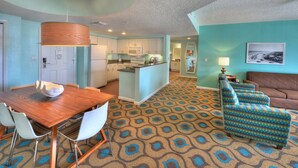 A modern kitchen with white cabinets, a central island, and a dining area with a wooden table and chairs.