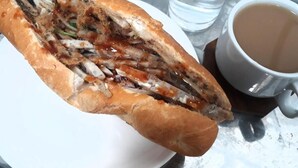 Un sándwich sobre un plato blanco, con un vaso de agua y una taza de café, todo sobre una bandeja metálica.