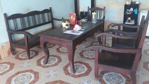 Un comedor con una mesa y sillas de madera, piso de baldosas y un estante con utensilios de cocina.