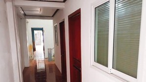 Un pasillo con una puerta roja, una ventana con persianas y suelo de baldosas.