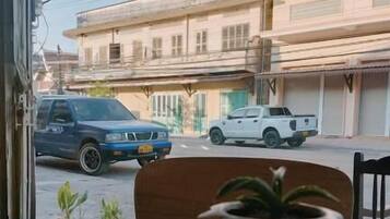 A table with a coffee cup and a potted plant, overlooking a street with parked cars and buildings.