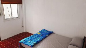 Una habitación pequeña con una cama individual, un cabecero de madera, una colcha azul estampada y una ventana con persiana marrón.