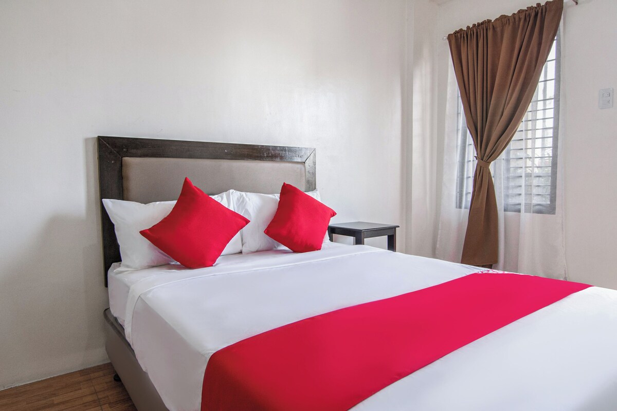 A neatly made bed with white and red bedding, a wooden headboard, and a small bedside table.