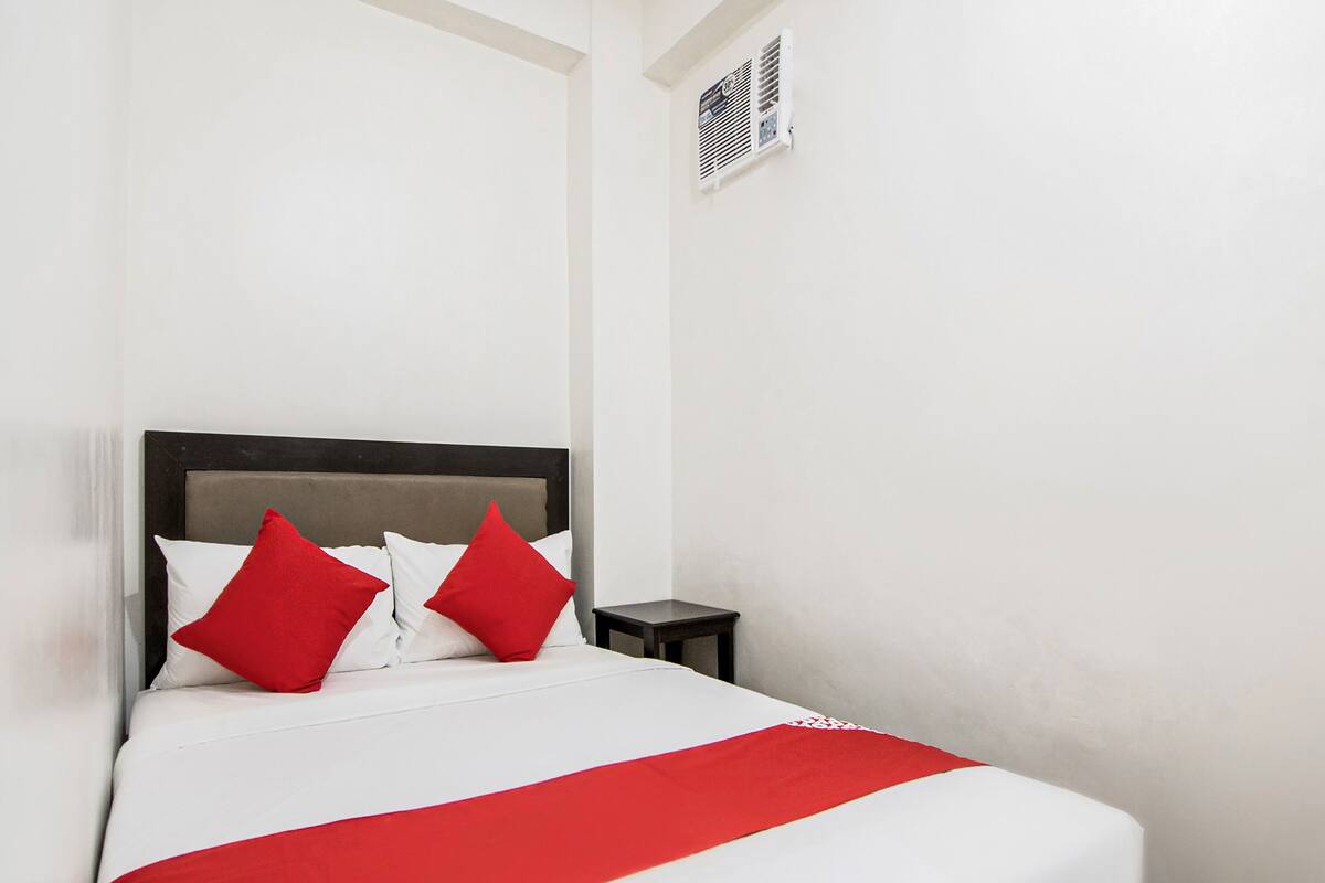 A bed with white and red bedding, a dark headboard, and a small bedside table.