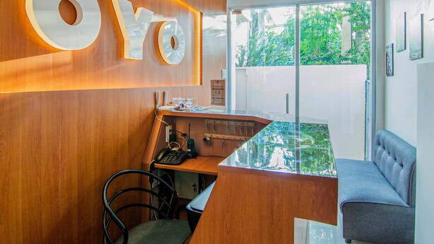 A modern office space with a wooden desk, a computer, and a chair. There is a large 'YO' sign on the wall and a window with a view of greenery outside. - OYO 431 Apollo 11 Apartelle (Pasay)