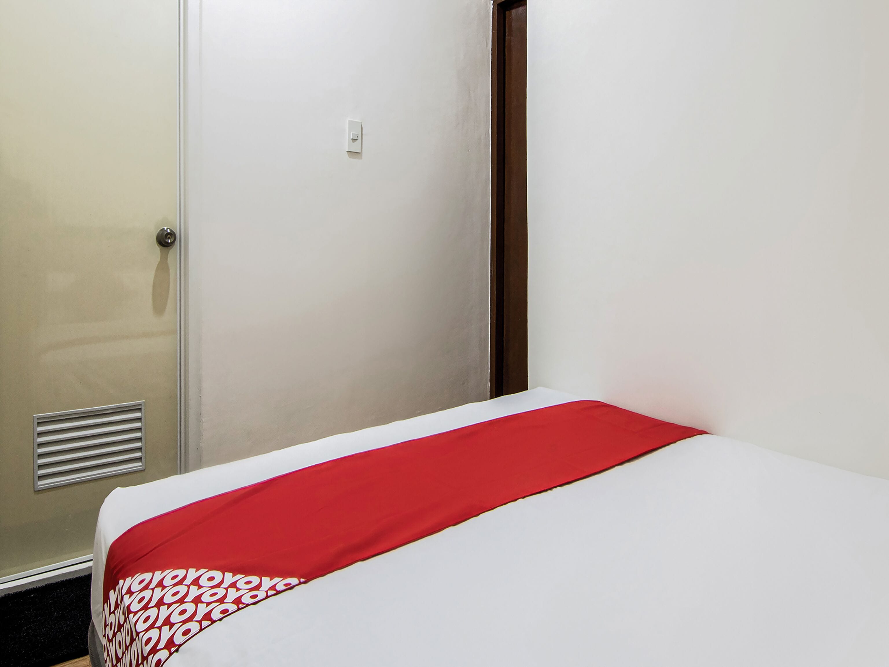 A hotel room with a bed, a door, and a vent.