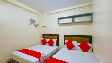 Habitación de hotel con dos camas individuales, cada una con cubrecamas y almohadas rojas y blancas. Hay un estante pequeño sobre las camas y un equipo de aire acondicionado en la pared.