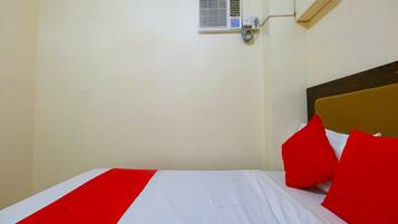 A hotel room with a bed, red and white bedding, a wall-mounted air conditioning unit, and a wooden headboard.