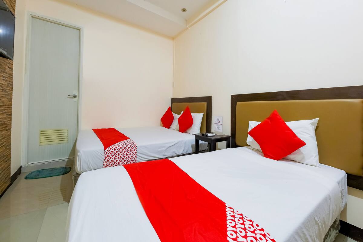 A hotel room with two beds, each with a red and white bedspread, a nightstand with a lamp, and a door with a vent.