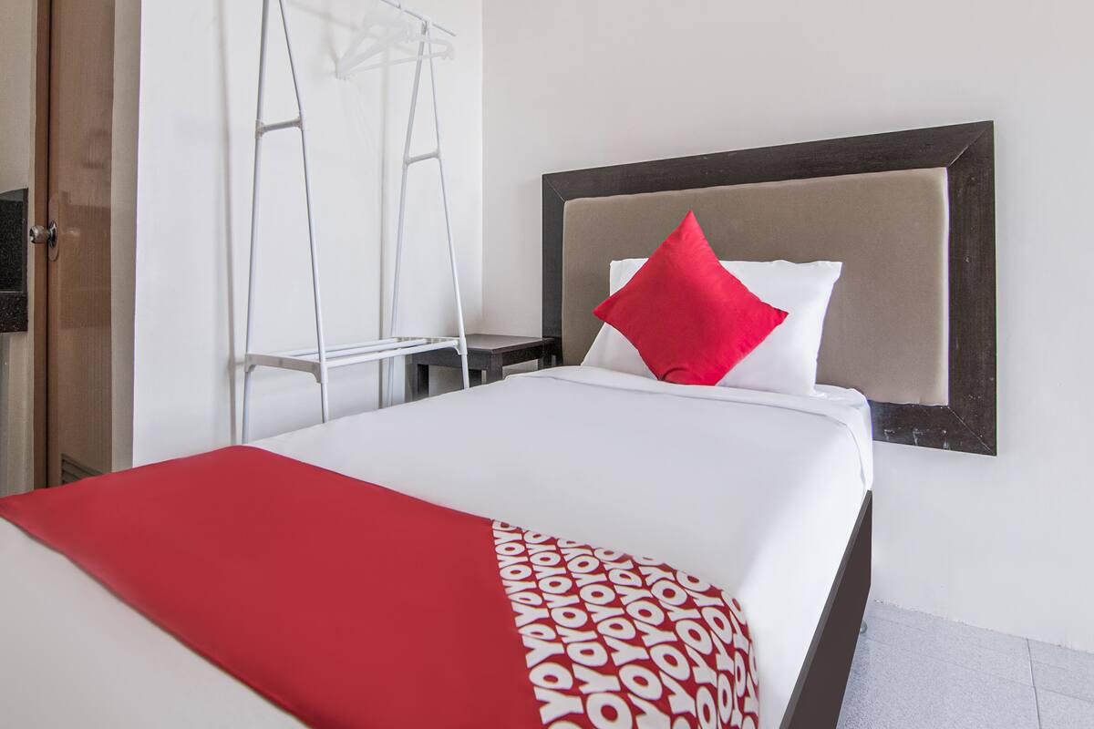 A hotel room with a bed, a red throw blanket, and a white pillow.