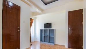 A spacious room with wooden flooring, a built-in TV shelf, and a large wooden door. - OYO 431 Apollo 11 Apartelle (Pasay)