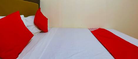 A bed with white sheets and red pillows, a wooden headboard, and a small blue shelf above it.