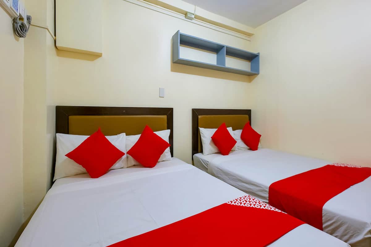 A hotel room with two beds, each with white bedding and red pillows, and a small shelf above the beds.