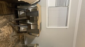 A dining area with a table and chairs, a window with blinds, and a decorative plant. - Pecan Orchard Bungalow (Purvis)