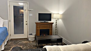 A hotel room with a bed, a television, a fireplace, a lamp, and a small table. - Pecan Orchard Bungalow (Purvis)