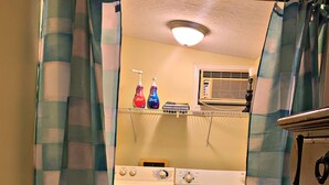 A laundry room with a washing machine, dryer, and a shelf with cleaning supplies. - Pecan Orchard Bungalow (Purvis)
