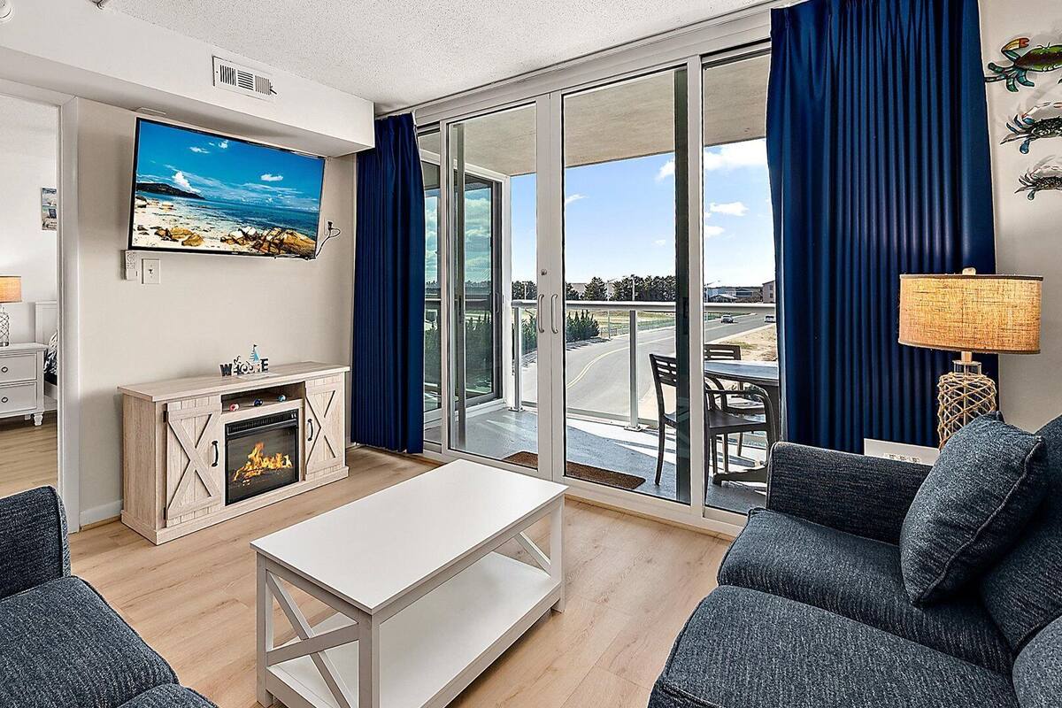 Ein modernes Wohnzimmer mit Kamin, Fernseher und Balkon mit Meerblick.
