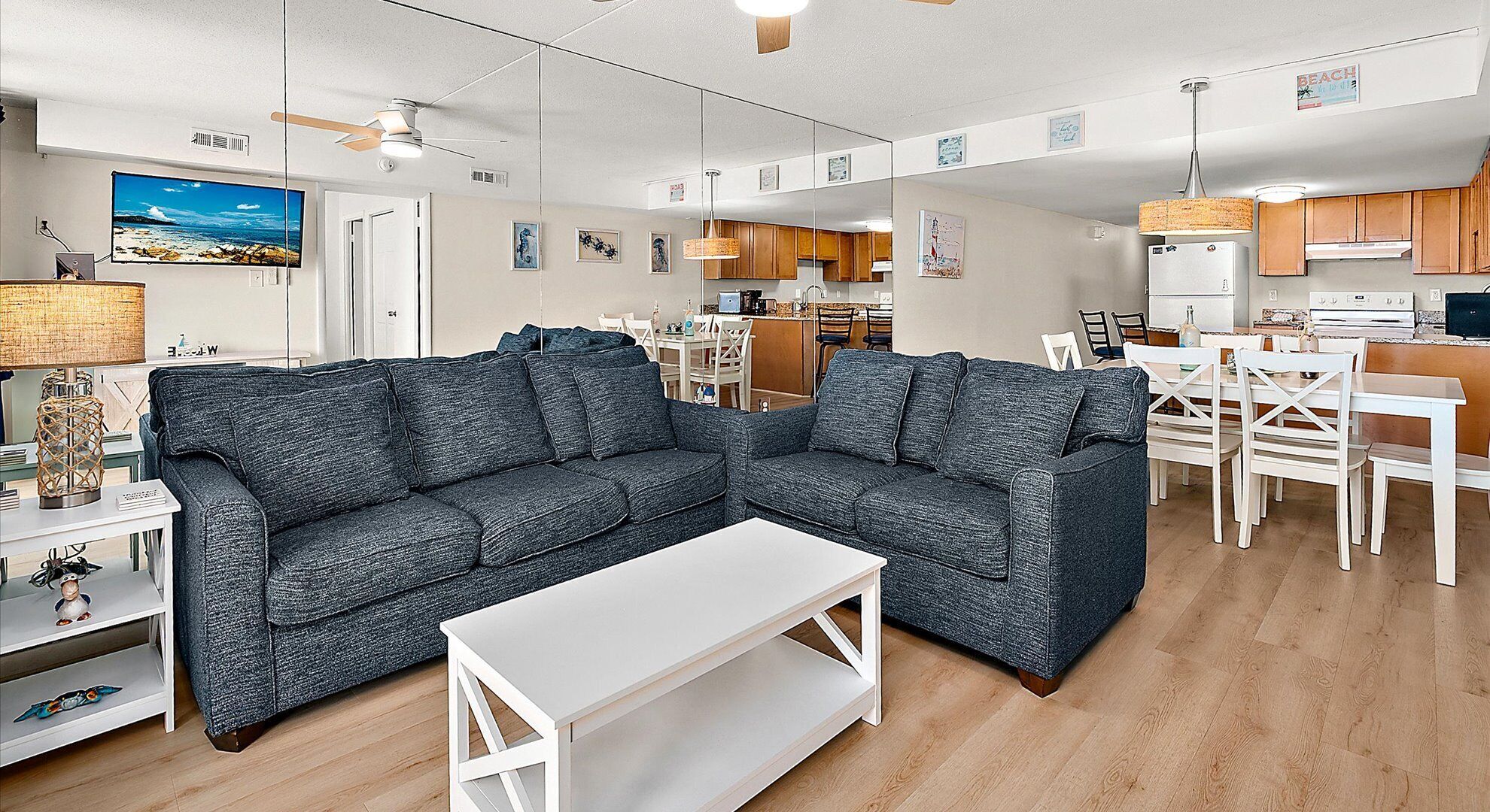 A modern living room with a sectional sofa, a white coffee table, and a dining area with white chairs and a wooden table.