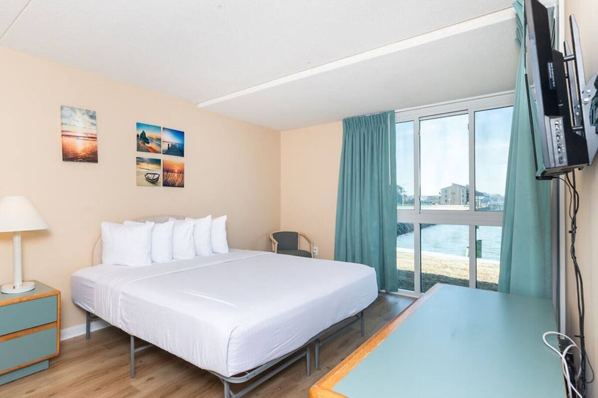 Ein Hotelzimmer mit Bett, Schreibtisch, Fernseher und einem Fenster mit Meerblick.