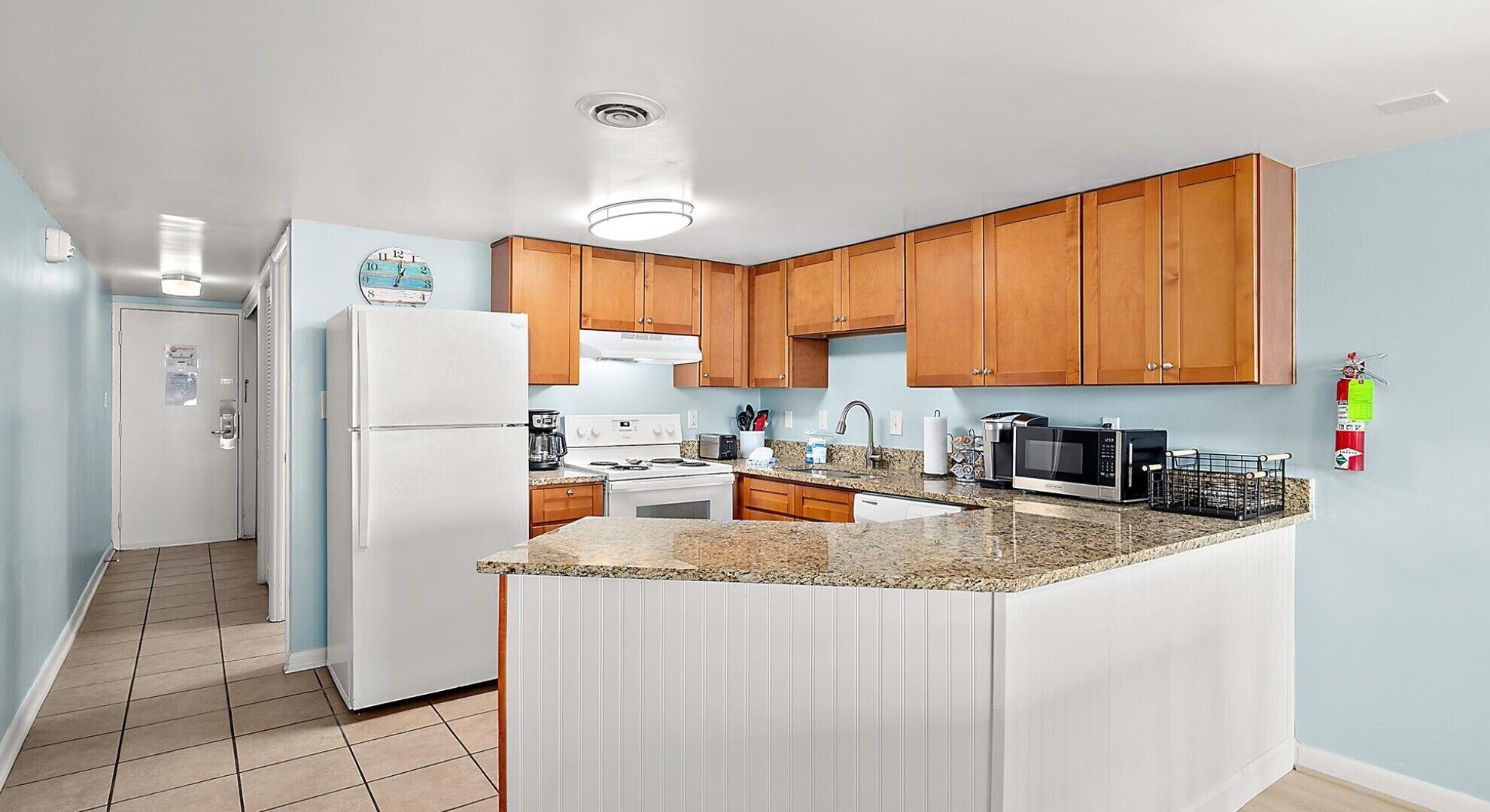 A kitchen with wooden cabinets, a white refrigerator, a stove, a microwave, and a granite countertop.