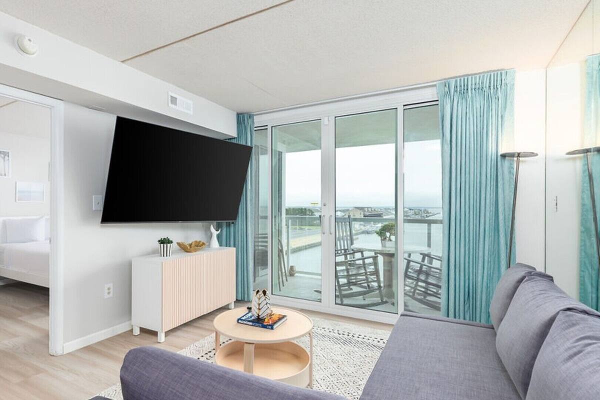 Ein modernes Wohnzimmer mit Flachbildfernseher, einer Couch, einem Couchtisch und einem Balkon mit Stadtblick.