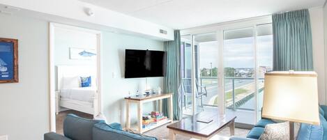Habitación de hotel con balcón, cama, televisor y zona de estar con mesa y sillas.