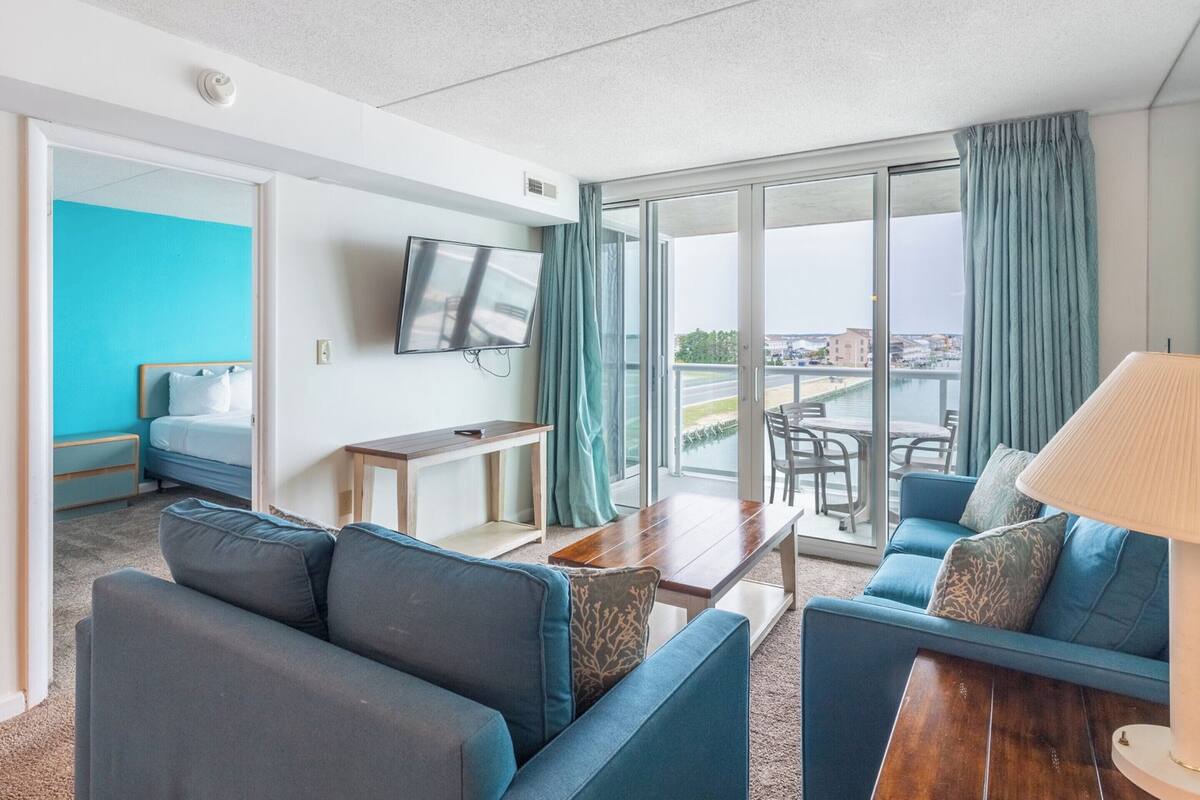 Ein modernes Hotelzimmer mit Balkon, Fernseher, einer Couch und einem Essbereich.