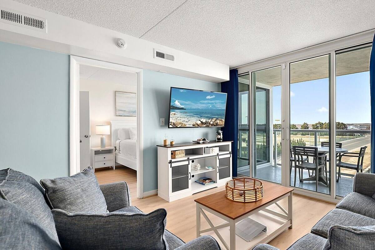 Ein modernes Wohnzimmer mit großem Fernseher, einem Balkon mit Sitzgelegenheit und Blick auf den Ozean.
