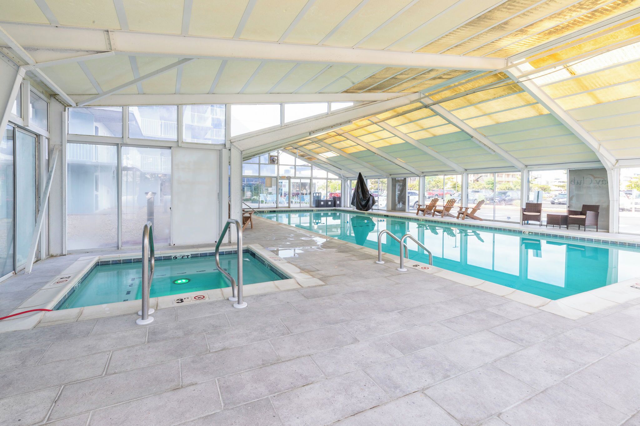 An indoor swimming pool with clear glass walls, a tiled floor, and a covered roof.
