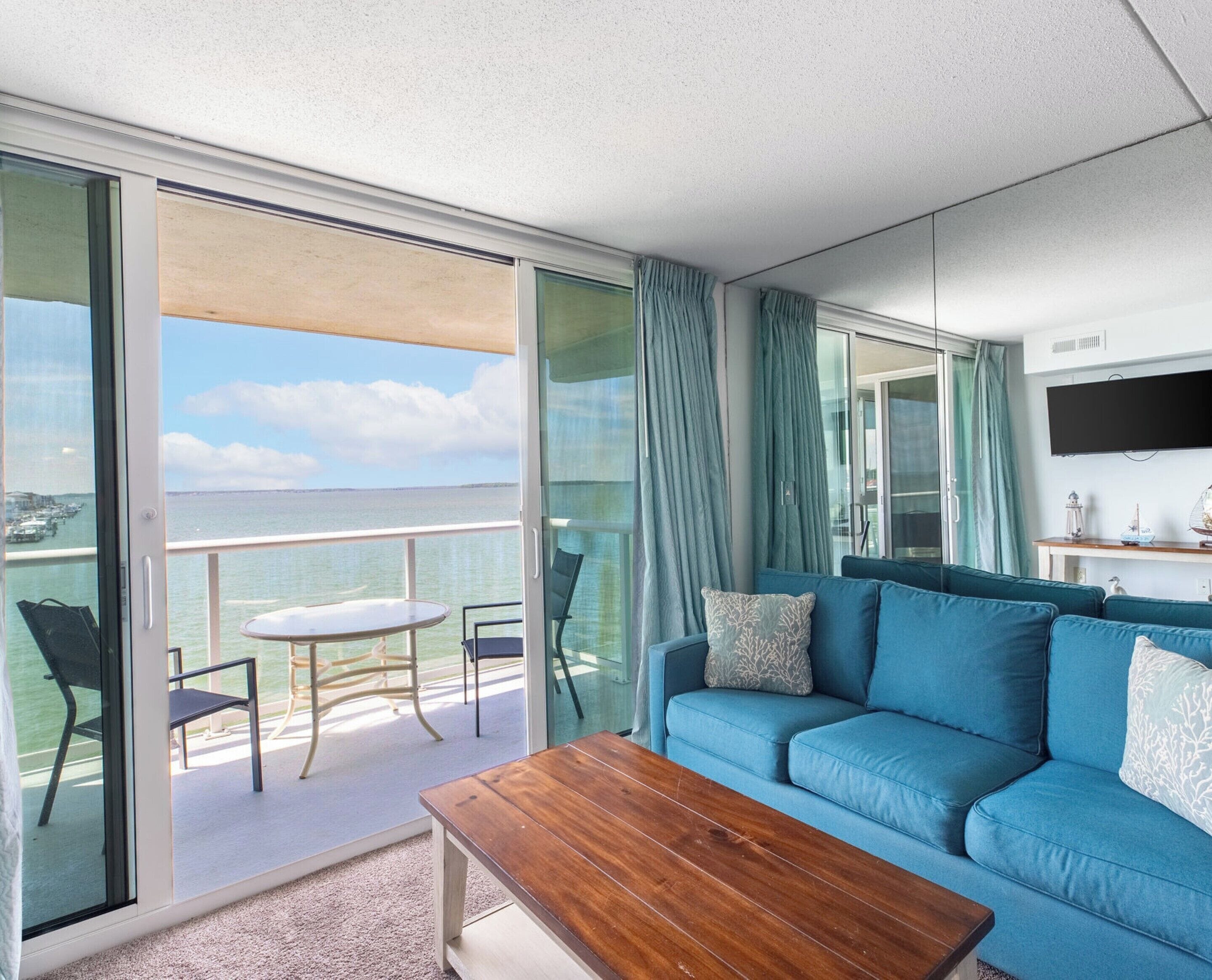 A balcony with a table and chairs, a blue sofa, and a TV mounted on the wall.