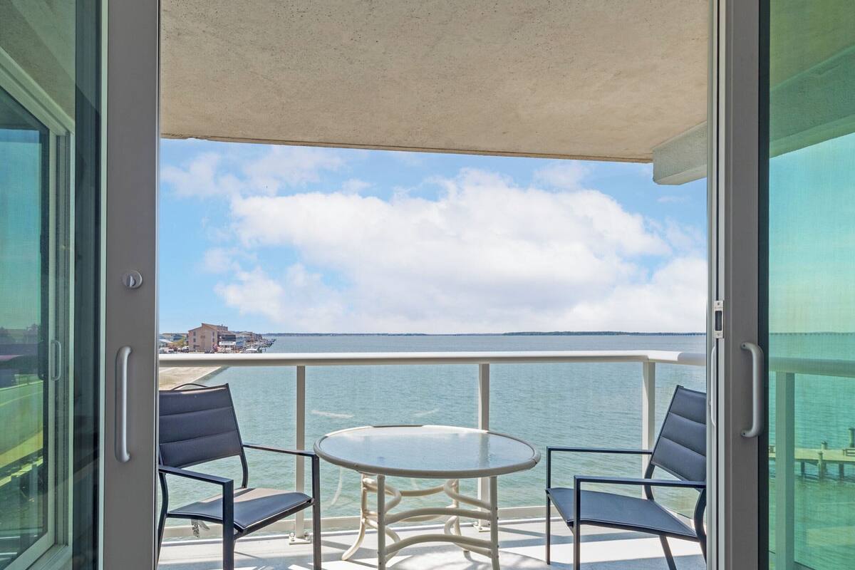 Ein offener Balkon mit Tisch und zwei Stühlen, mit Blick auf ein ruhiges Meer und eine entfernte Küste.