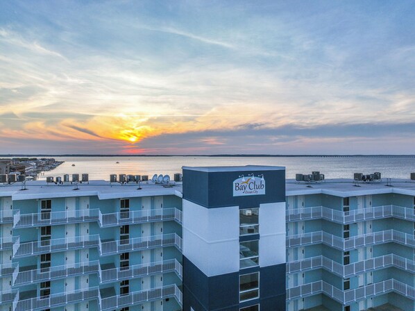 Un hotel de varios pisos con balcones, vista al océano y un atardecer de fondo.