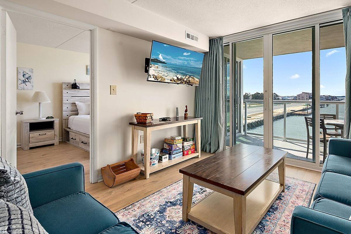 Ein modernes Wohnzimmer mit einer Couch, einem Couchtisch, einem an der Wand montierten Fernseher und Meerblick durch große Fenster.