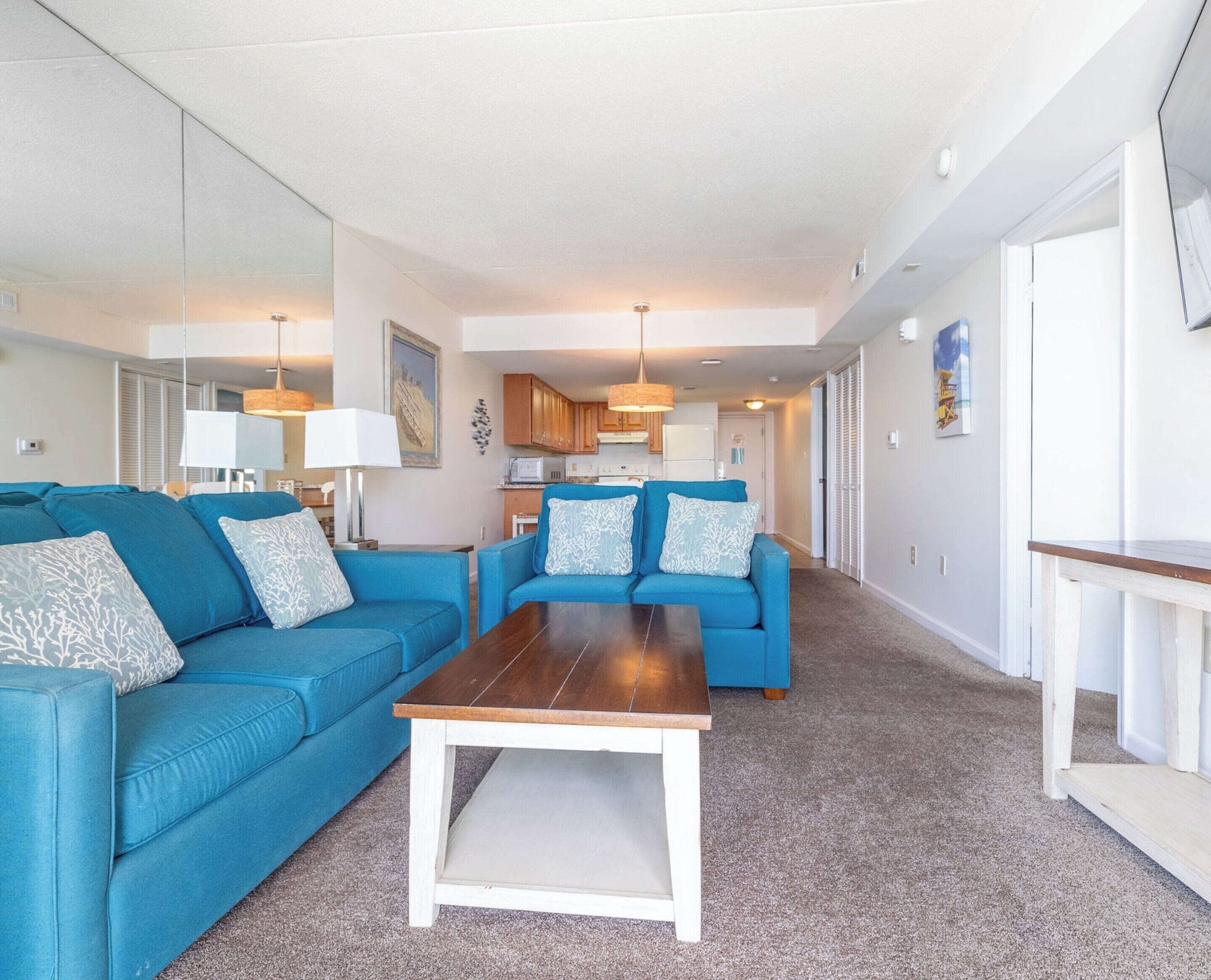 A living room with two blue sofas, a wooden coffee table, and a kitchen in the background.