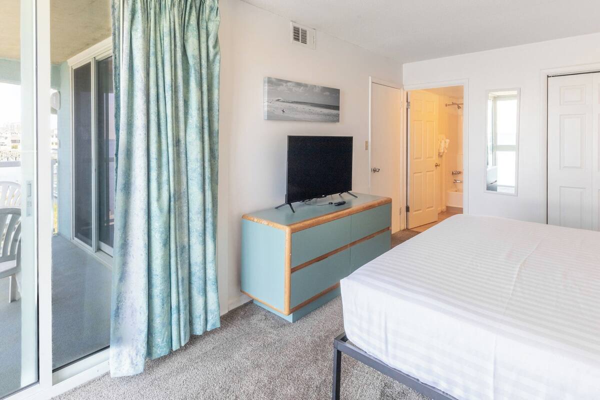 Ein Hotelzimmer mit Bett, Fernseher auf einer Holzkommode, einer Schiebetür und einem sichtbaren Badezimmer durch eine geöffnete Tür.