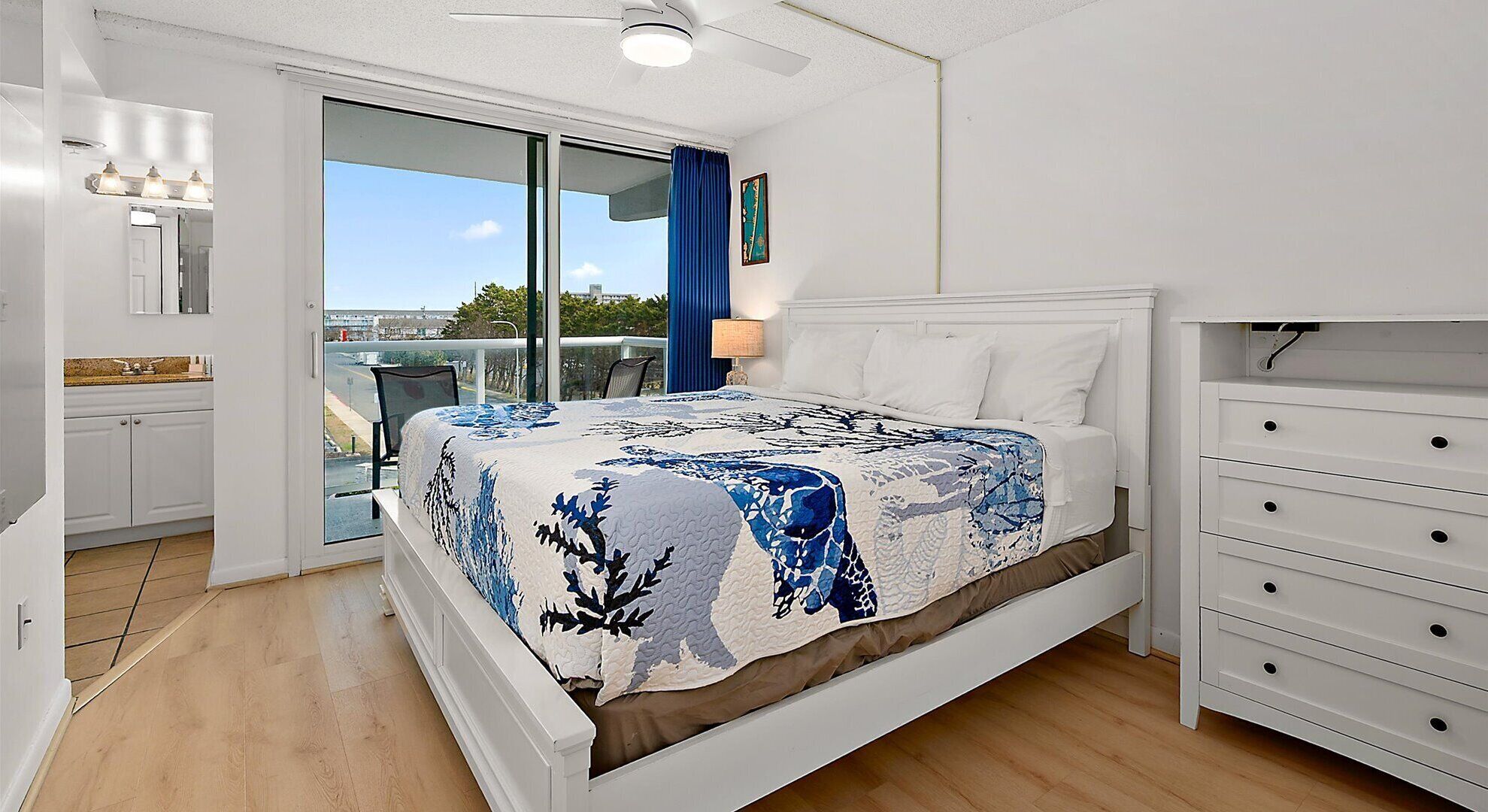 Een slaapkamer met een bed, een nachtkastje, een dressoir en uitzicht door een schuifdeur.