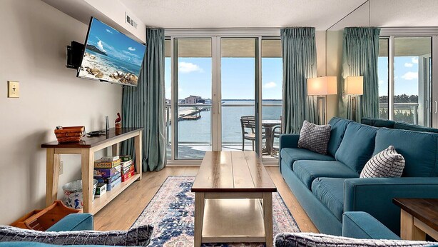 Een moderne woonkamer met een grote televisie, een bank, een salontafel en uitzicht op de zee.