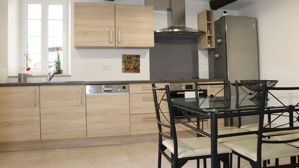 A modern kitchen with wooden cabinets, a stainless steel refrigerator, and a glass dining table with chairs.