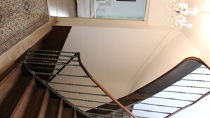 A spiral staircase with wooden steps and metal railings, leading to a landing with a view of the sky.