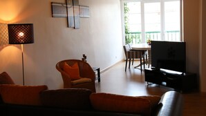 A living room with a sofa, a chair, a TV, and a dining area with a table and chairs.