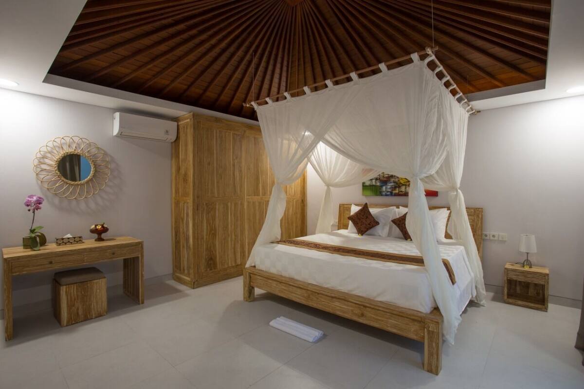 A bedroom with a four-poster bed, a wooden desk, a mirror, and a bedside table with a lamp.