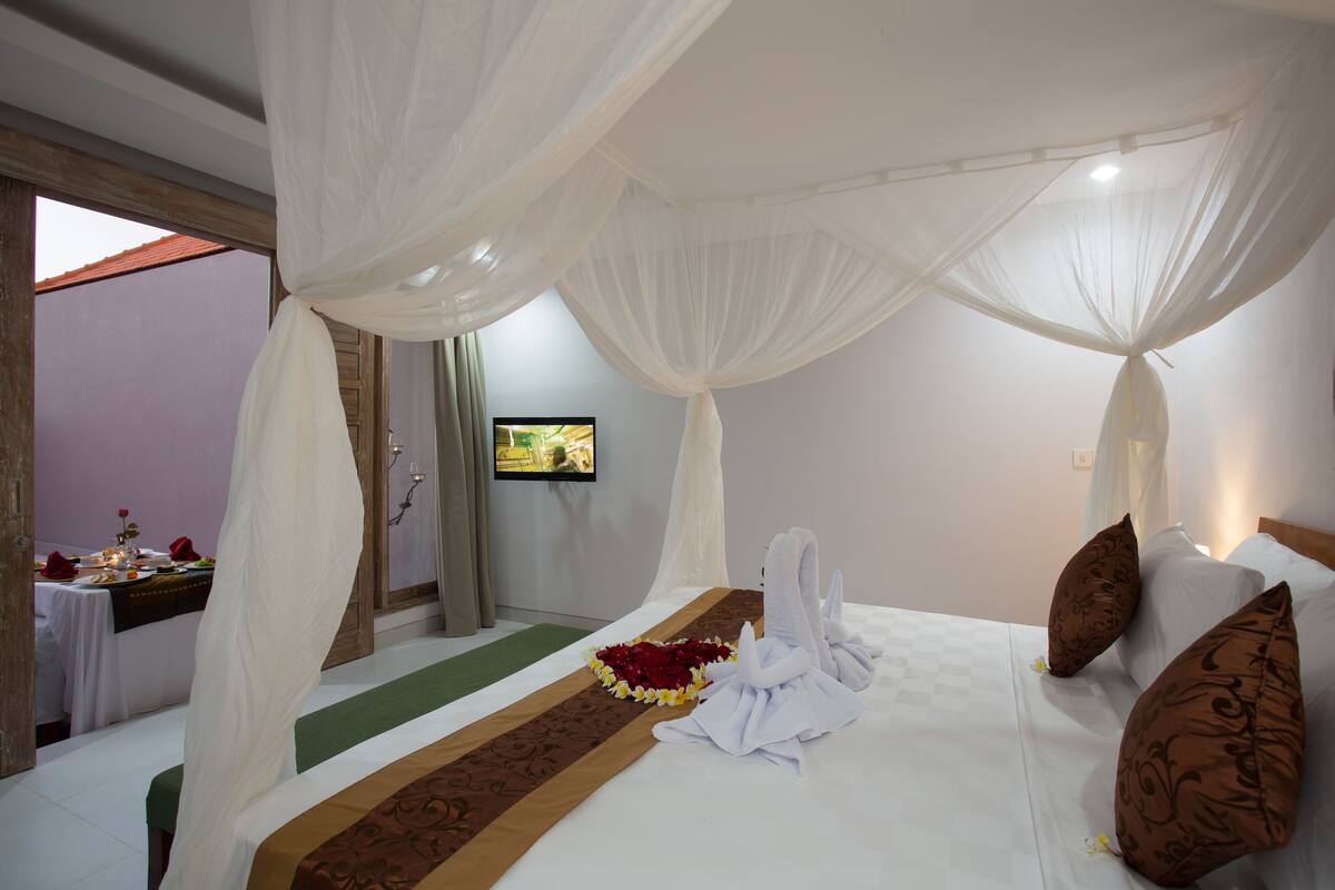 A hotel room with a bed, white canopy, and a green carpet.
