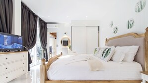 Quarto bem organizado com cama de madeira, roupa de cama branca e uma televisão sobre um penteadeira.