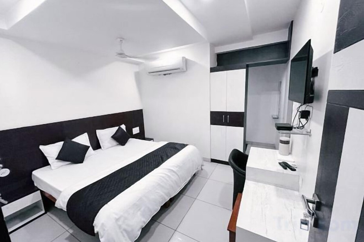 A modern hotel room with a bed, a desk, a chair, a flat-screen TV, and a mirror.