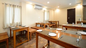 A conference room with wooden tables and chairs, an air conditioning unit, and a door. - Hotel Rashika Palace (Jaipur)