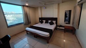 A hotel room with a large bed, a desk, a chair, a ceiling fan, and a window with a city view. - Hotel Rashika Palace (Jaipur)