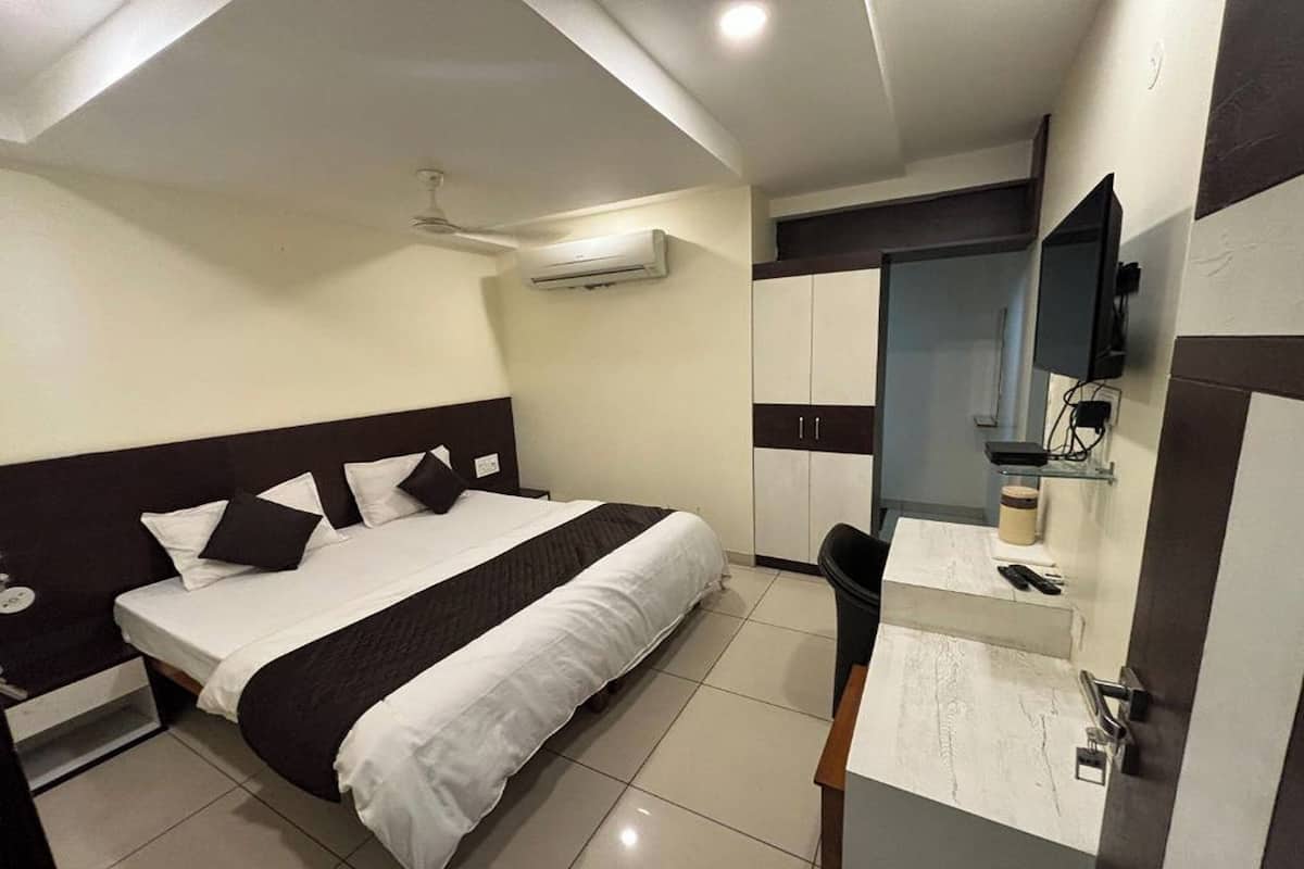 A hotel room with a bed, bedside table, air conditioning unit, wardrobe, and a mirror.